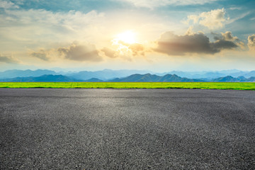 Empty asphalt road and green mountain landscape at sunset.