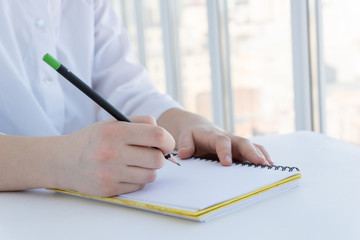 young female in white clothers writes in white notebook, doctor writes its perscriptions, student is studying, or remote work concept