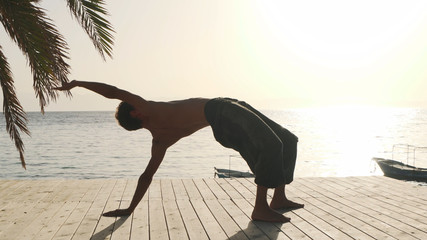 Flexible caucasian man practicing yoga at seashore at sunrise