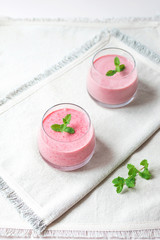 Two glasses of homemade berry smoothie decorated with mint leaves over white napkins in the kitchen. Healthy food concept.