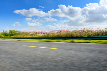 Motion blurred asphalt road and container port terminal landscape under blue sky.