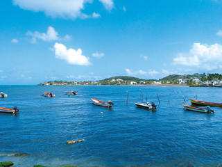 Fototapeta na wymiar Turquoise waters of the Caribbean Sea with traditional fishing boats and the silhouette of a small town in the background. Idyllic tropical landscape. Authentic Caribbean spot.