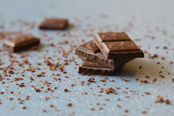 Macro photo of Broken pieces Chocolate bar. Dark chocolate stack with brown powder on a stone background with copy space.
