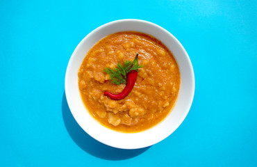 Famous traditional Arabic cuisine - peeled fava beans with chili in white bowl on blue background. Top view. Foul Mudammas, egyptian beans.