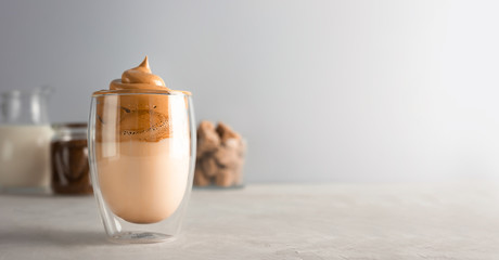 Trend korean drink with foam. Glass with Dalgona frothy coffee on grey table. Banner with copy space.