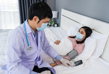 doctor measuring blood pressure of sick woman in bed, people must be wearing medical mask protecting from coronavirus(covid-19) pandemic