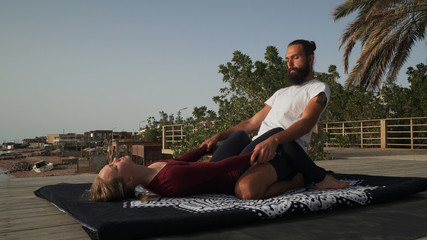 Handsome bearded man doing thai yoga massage for a woman at sunset seashore. © Alexander Belinskiy