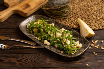 Fresh green salad of arugula, pear, goat cheese and pine nuts seasoned with honey. Healthy salad for breakfast.