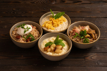 Four types of cereal for breakfast. Oat, buckwheat, pearl barley and rice porridge with various additional ingredients on a dark wooden table.