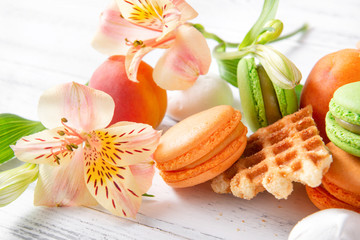 Fototapeta na wymiar peach, green macaroon cookies with yellow Alstroemeria flowers, apricots, waffle on a beige background