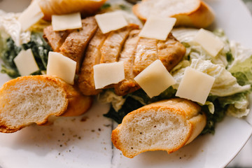 Caesar salad in a beautiful plate stands on a wooden table in a cafe on a sunny day. Caesar with chicken and white bread croutons with parmesan and anchovy dressing. 