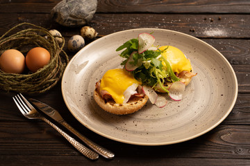 Poached eggs with bacon, radish, arugula and a burger bun are beautifully served on a dark wooden table. Healthy breakfast of salad eggs and vegetables.