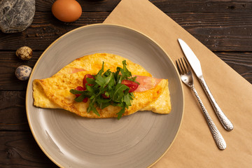 Omelet with bacon, cherry tomatoes and arugula are beautifully served on a dark wooden table. Healthy breakfast made from eggs of salad and vegetables, top view.