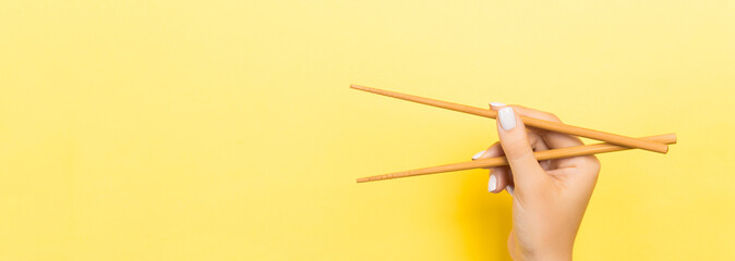 Wooden chopsticks holded with female hands on yellow background. Ready for eating concepts with...