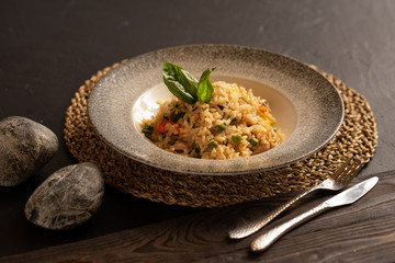 Risotto with chicken and vegetables, garnished with basil leaves, are beautifully preserved by cutlery against a dark background.