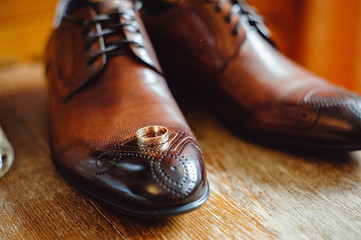 Stylish men's brown shoes with a pattern on a wooden background.The wedding ring is on the shoes. Wedding accessories groom on wooden background.