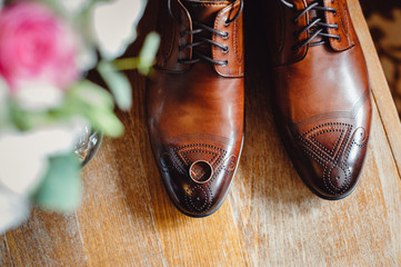 Stylish men's brown shoes with a pattern on a wooden background.The wedding ring is on the shoes. Wedding accessories groom on wooden background. Film noise