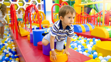 Cute little boy crawling and playing on colorful playground at shopping mall