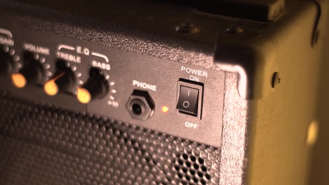 Turn on the guitar combo. Finger press button. Close-up.