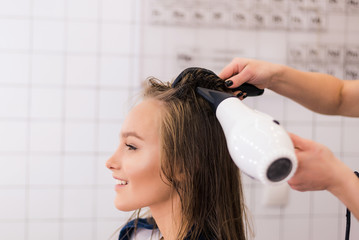 Professional woman hairdresser drying woman's hair styling using blow dryer at the hairdressing...
