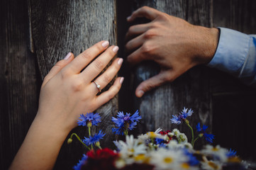 Obraz na płótnie Canvas The hands of a man and a woman open the old wooden door. Close-up. Gold wedding ring on the bride's finger, on the background of gray doors. Selective focus.