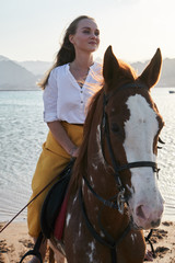 Obraz premium View of young girl sits on a horse in nature at sunset