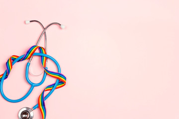 Stethoscope with LGBT rainbow ribbon on pink background.