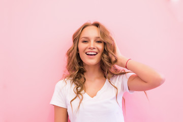 Blonde woman with curly beautiful hair smiling isolated on pink background.