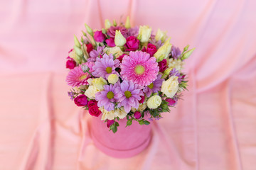 A joyful bouquet of fresh flowers in a pink paper box on a pink background (Colors: white, pink, lilac, red, green, fuchsia. Flowers: eustoma, rose, chrysanthemum, gerbera)