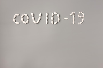 COVID-19 flu epidemic. The inscription Covid-19 of pills on gray background, Flat lay, copy space.