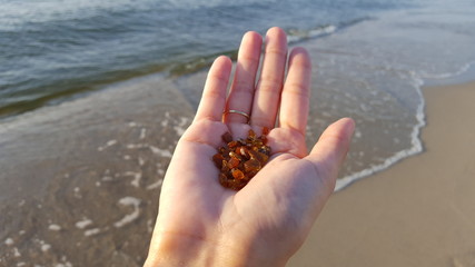 Amber on female palm against the sandy beach. Transparent bright pieces of amber in hands. Natural mineral is a frozen ancient resin. Sunstone. Jewelry amber.