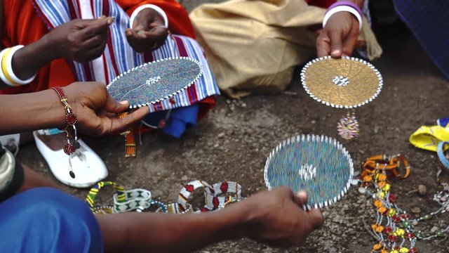 Hands of Masai Women with Traditional Jewelry sell their homemade souvenirs just on the Ground Showing them for Tourist and Travellers