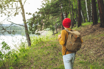 Naklejka premium Tourist with a backpack and a red hat is walking in the forest among the trees. Active trekking and unity with nature