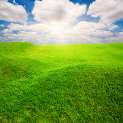 Obraz na płótnie Canvas Green grass field on small hills and blue sky with clouds