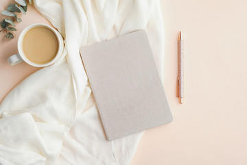 Flat lay composition with paper notebook, cup of coffee, blanket and pen on beige background. Elegant feminine workspace, home office desk concept.