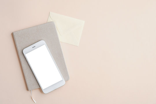 Flat lay, top view office desk table with mobile phone mockup with blank white screen, paper notebook and envelope on beige background. Business and technology concept.