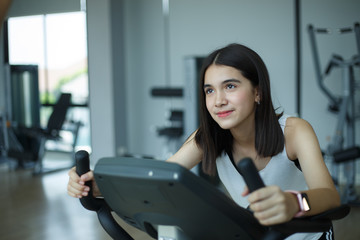 Fototapeta na wymiar Fit young girl using exercise bike at the gym. Fitness female using air bike at gym.