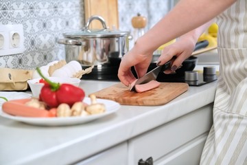 Close-up of womans hands preparing food in the kitchen, cutting sausages with knife