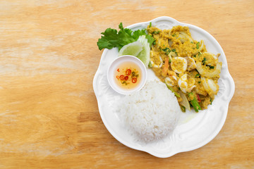 Stir fried squid in curry powder with rice and fish sauce mixed chili in white dish on wooden table.