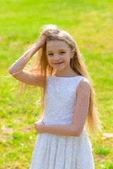 Obraz premium Beautiful blue-eyed girl with long blond hair in a white dress walking in the flower garden. summer bright, emotional photo.
