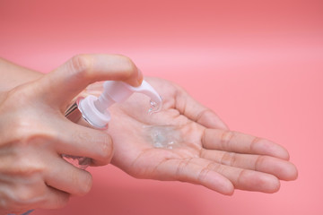 Woman hands using wash hand sanitizer gel pump dispenser. Clear sanitizer in pump bottle, for killing germs, bacteria and virus, pink background.