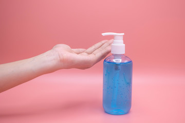 Woman hands using wash hand sanitizer gel pump dispenser. Clear sanitizer in pump bottle, for killing germs, bacteria and virus, pink background.