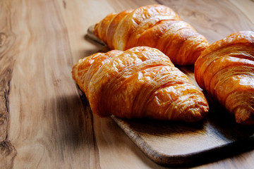 Top view shot of appealing plain mini croissants baked to golden crisp served on cutting board, exotic wood textured backgroud. Traditional french pastry. Close up, copy space.