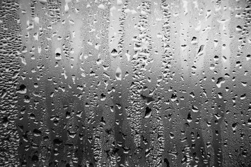 Black and white background depicting raindrops running down the glass on the window in a dark sad cloudy weather. Melancholy.