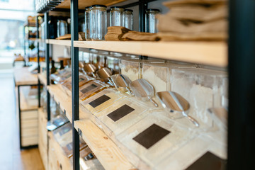 Zero waste shop interior details. Wooden shelves with different food goods and personal hygiene or cosmetics products in plastic free grocery store. Eco-friendly shopping at local small businesses.