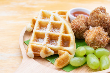 Waffles with fried chicken ball and grape in wooden dish on wooden table.