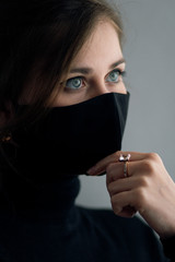 portrait of young beautiful woman in protective black stylish mask with hand with jewelry under her chin, lifestyle 2020 under quarantine and epidemic, fashion disease