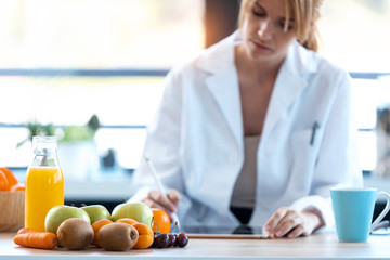 Woman nutritionist doctor working with her digital tablet for doing a diet plan in the consultation.