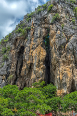 view of Wat Tham Khao Yoi Cave, Buddhist temple with green tree and rock mountain background, in Phetchaburi, Thailand with Thai text banner means the name of this local is Wat Tham Chao Yoi Cave.