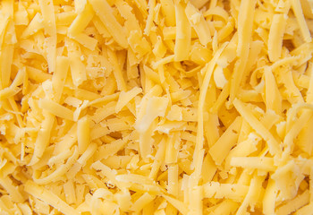Cheese grated on a grater lies in a pile on the Board. There's a whole piece of cheese next to it. Yellow cheese.